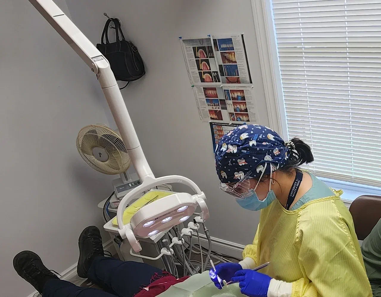 A masked dental clinician wearing a patterned surgical cap and purple gloves treats a patient at Milton Dental Clinic