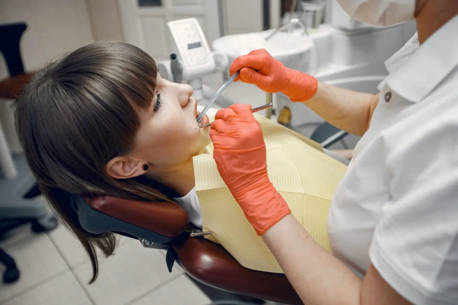 A dental professional examines a patient reclining in a dental chair