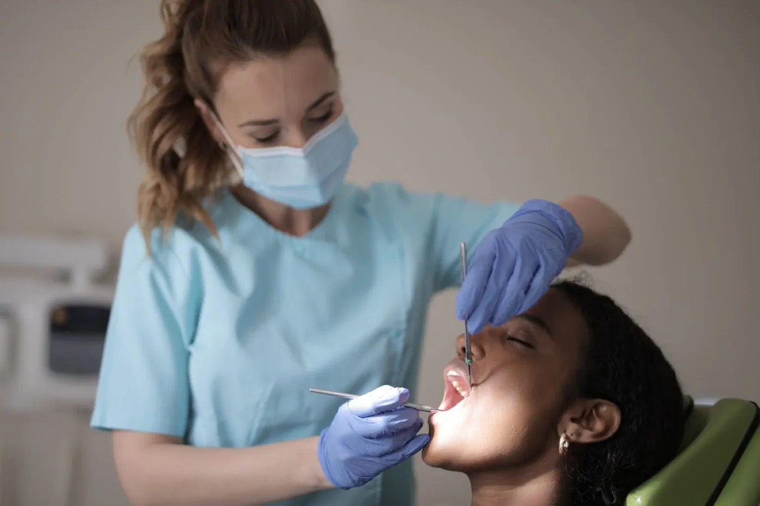 A masked dental clinician examines a patient under a treatment light